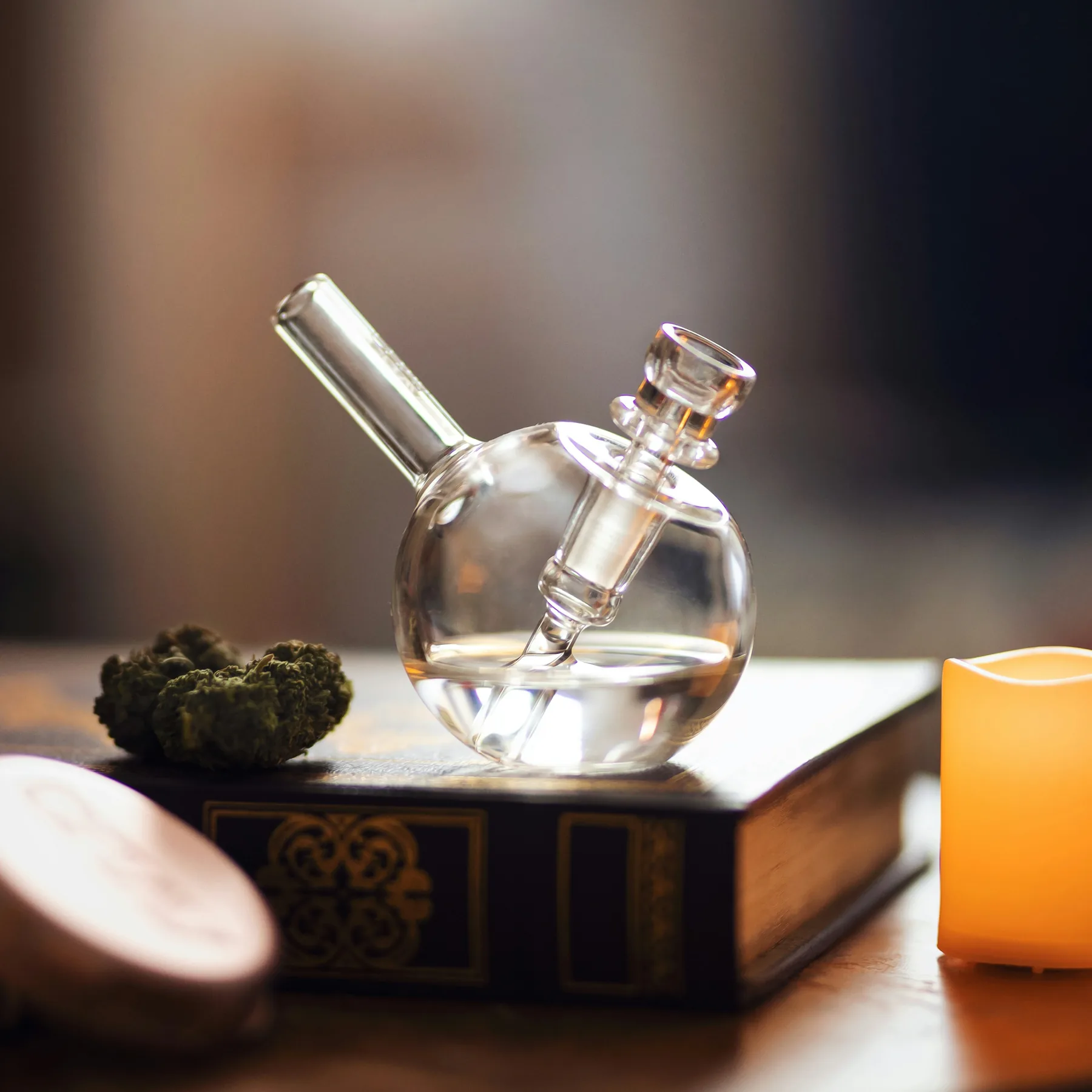 Glass cannabis accessory arranged on books beside a warm light